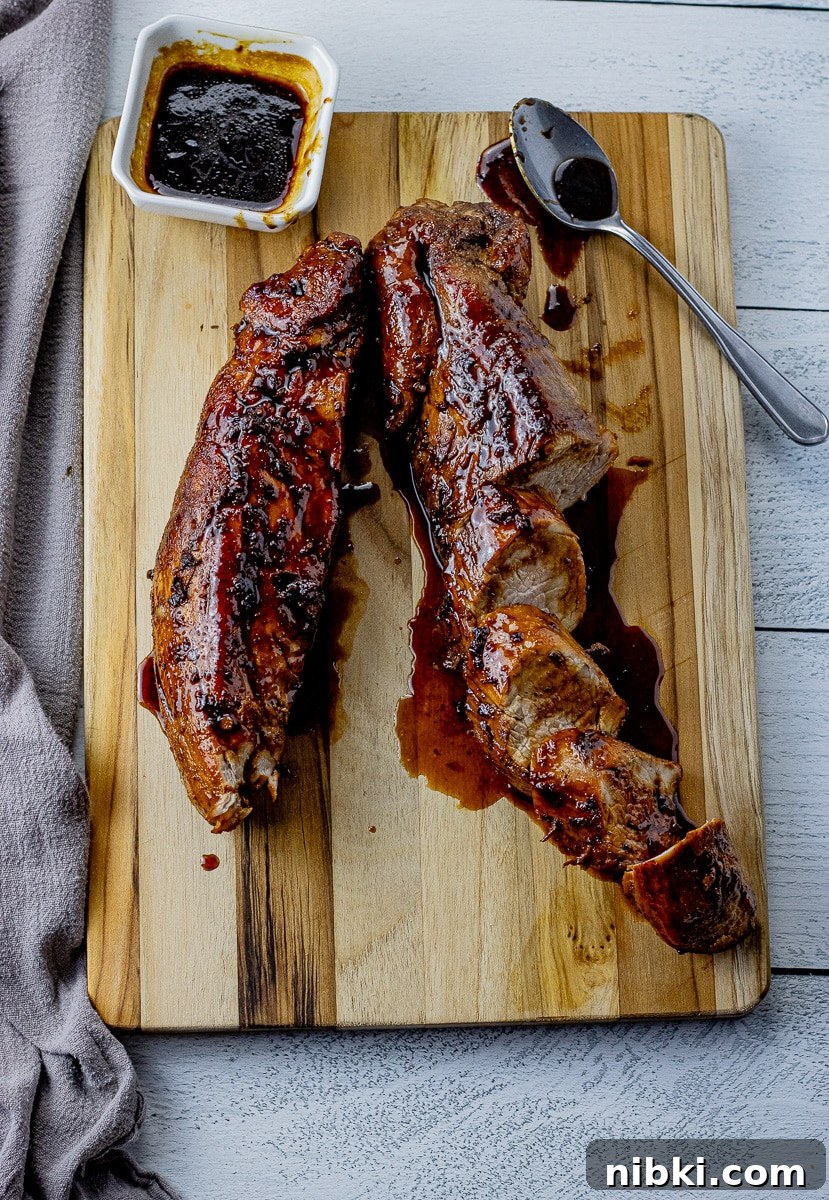 two pork tenderloins on a wooden cutting board, one sliced and drizzled with a maple glaze