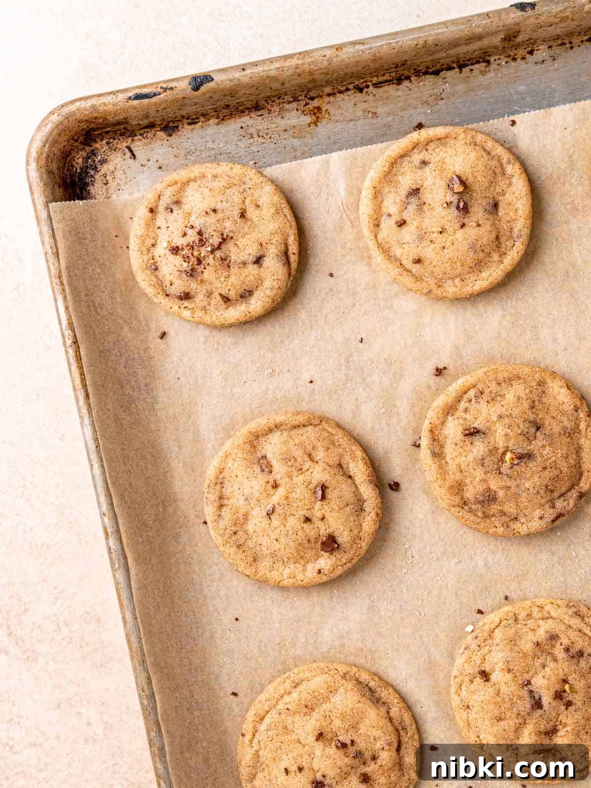 Browned Butter Snickerdoodles with Cinnamon Sugar 9 Baked snickerdoodle cookies on a parchment-lined sheet.