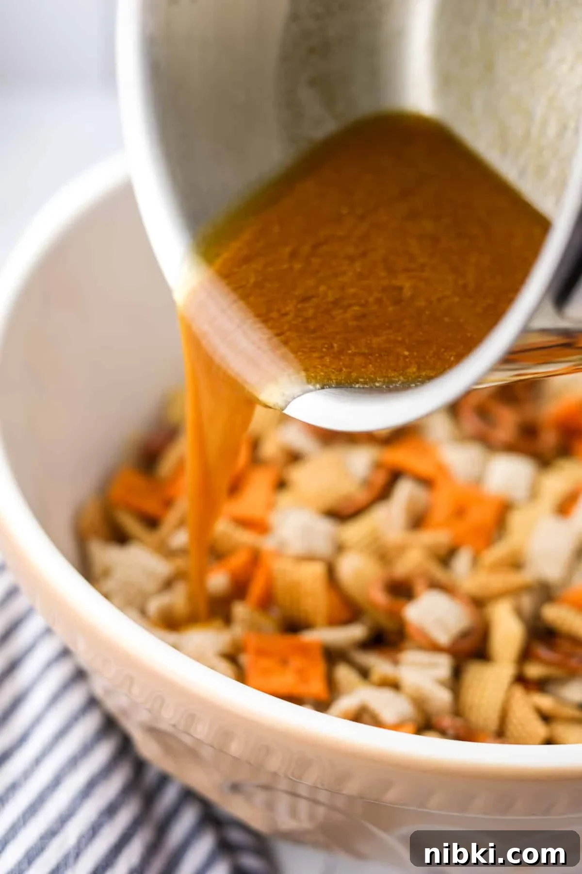 Homemade Chex Mix: Savory Snack Mix Recipe 6 Pouring melted butter into a bowl of snack mix.