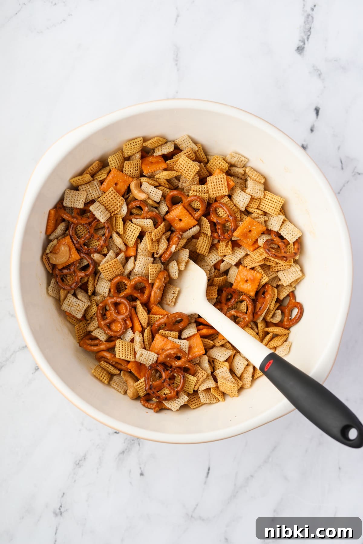 Homemade Chex Mix: Savory Snack Mix Recipe 7 A bowl of chex mix being stirred with a silicone spatula.