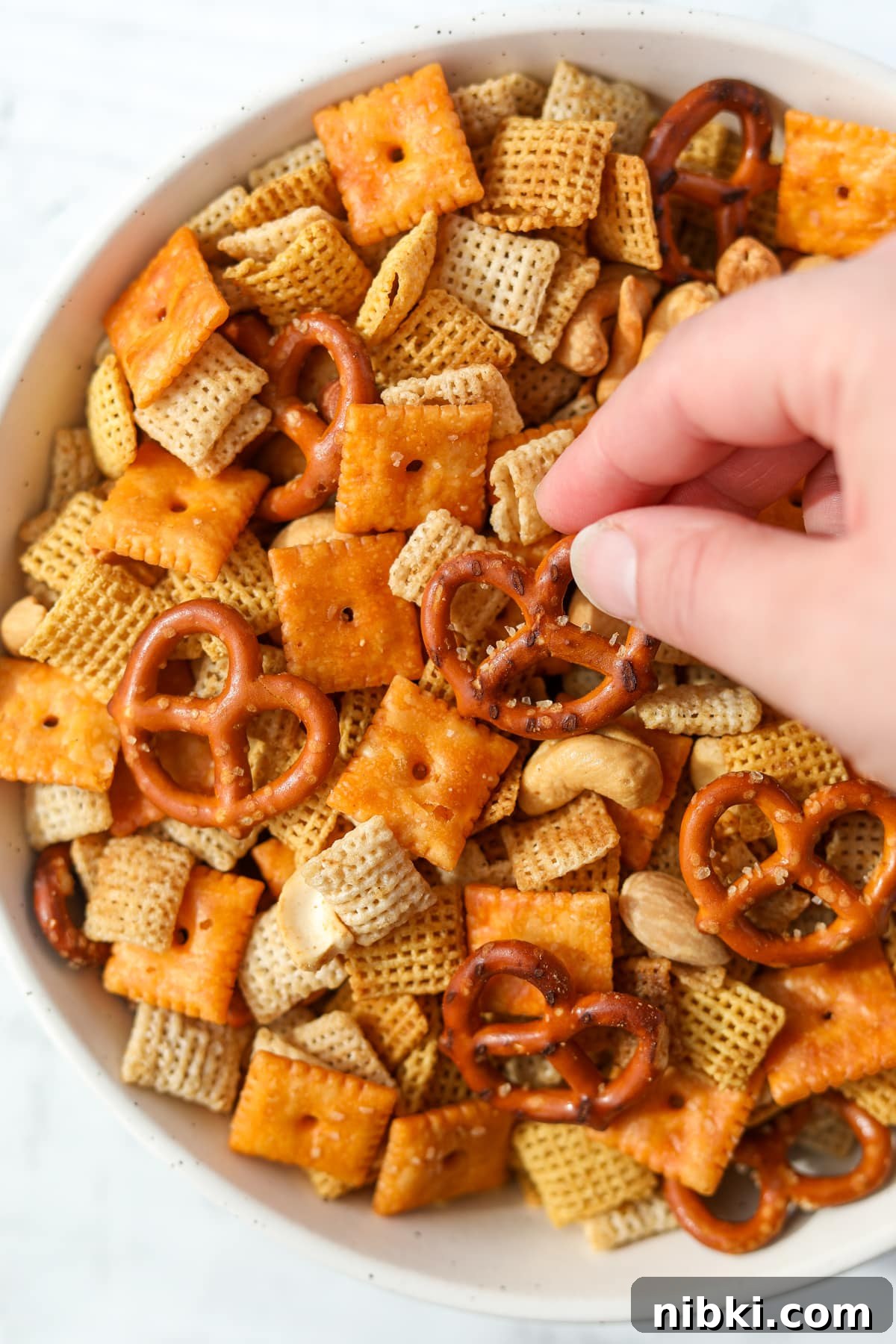 Homemade Chex Mix: Savory Snack Mix Recipe 10 Taking a pretzel from a bowl of snack mix.