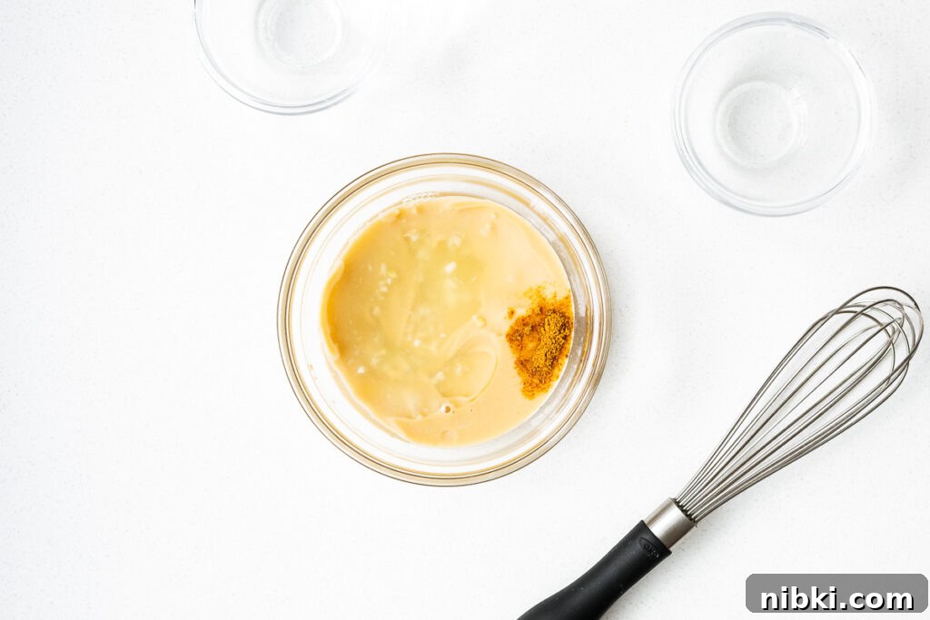 Tahini sauce ingredients in a small glass bowl next to an unused whisk.