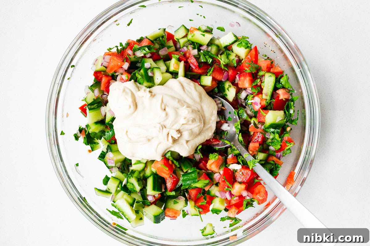 Israeli chopped salad (Jerusalem salad) topped with tahini sauce in a glass bowl before mixing.