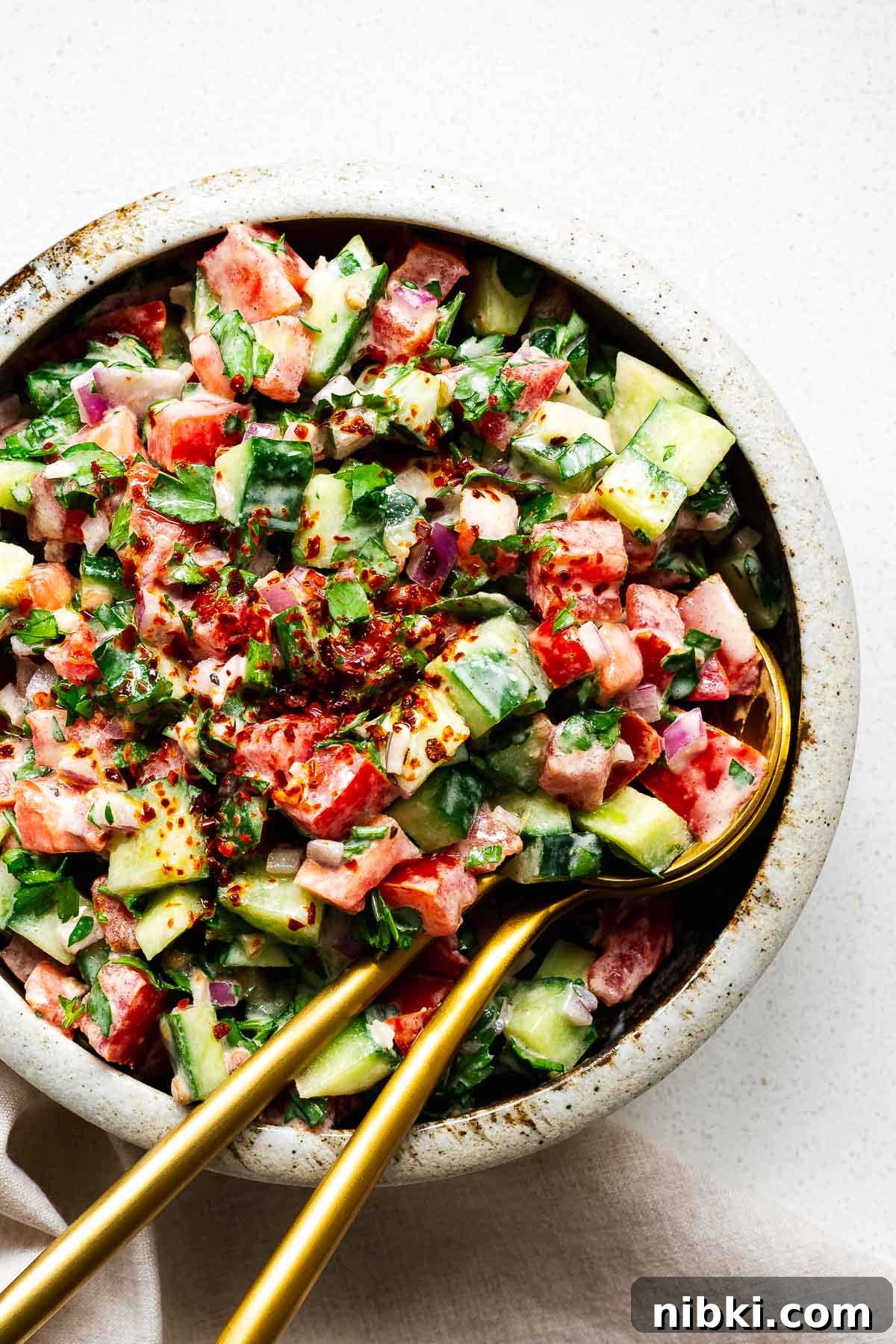 Middle Eastern tahini salad in a bowl with gold serving spoons.