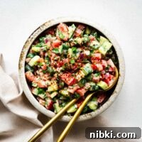Jerusalem salad (Israeli salad) with tahini sauce in a bowl with golden serving spoons viewed from above.