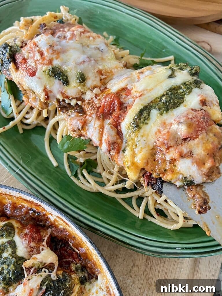 Skillet Chicken Parmesan with Pesto 11 Placing parmigiana di pollo over pasta in green platter.