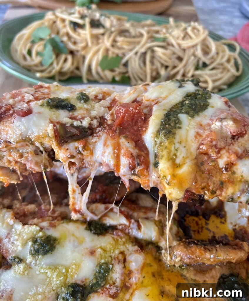Skillet Chicken Parmesan with Pesto 3 Chicken parmesan on spatula about to be placed on pasta in background.
