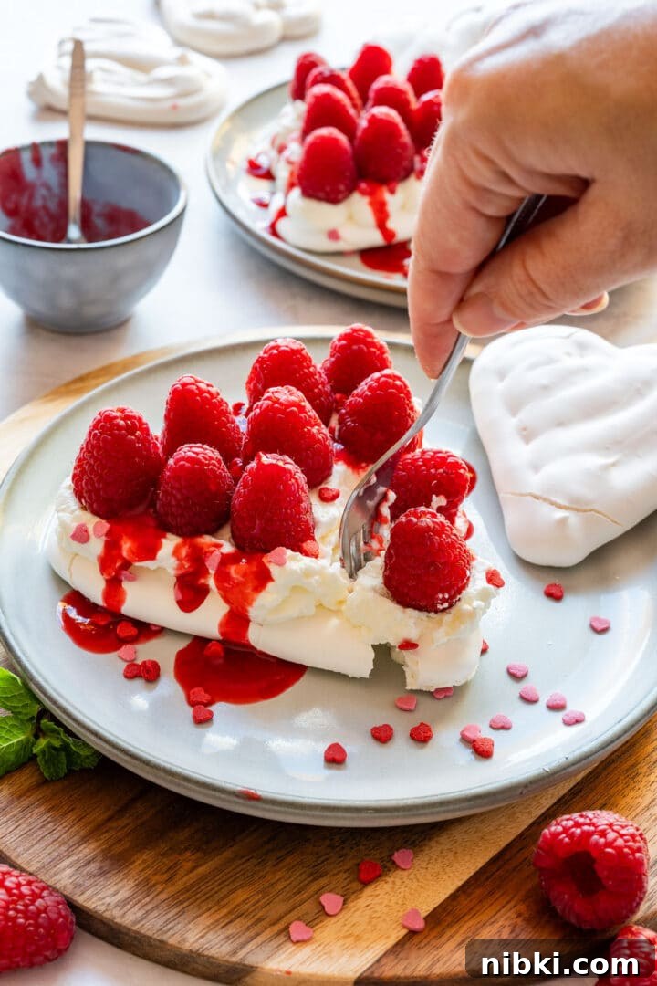 Cutting into a pavlova heart topped with whipped cream, raspberries and raspberry coulis.