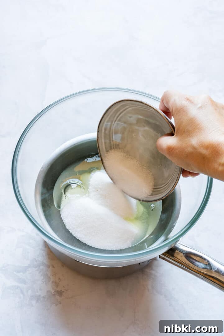 Adding sugar to egg whites in a heatproof bowl set over simmering water.
