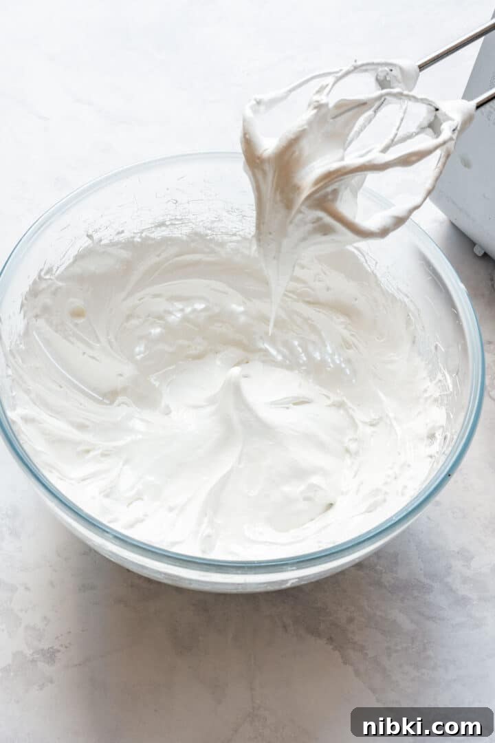 Glossy Swiss meringue whipped to thick peaks in a mixing bowl.