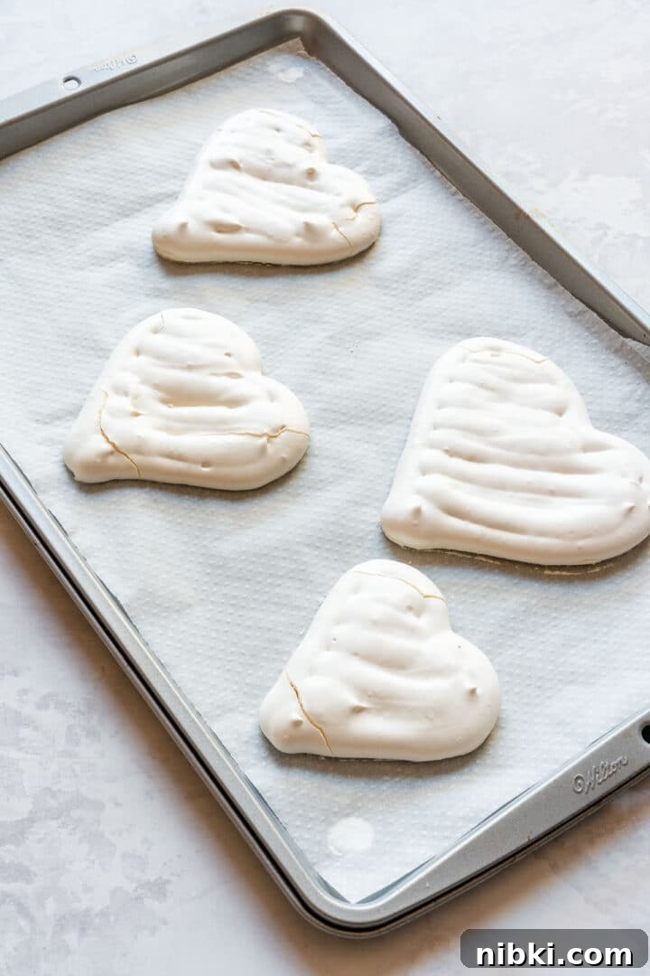 Baked meringue hearts cooling on a parchment-lined baking sheet.