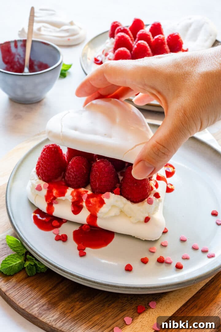 Stacking two meringue hearts with whipped cream and raspberries in the middle.