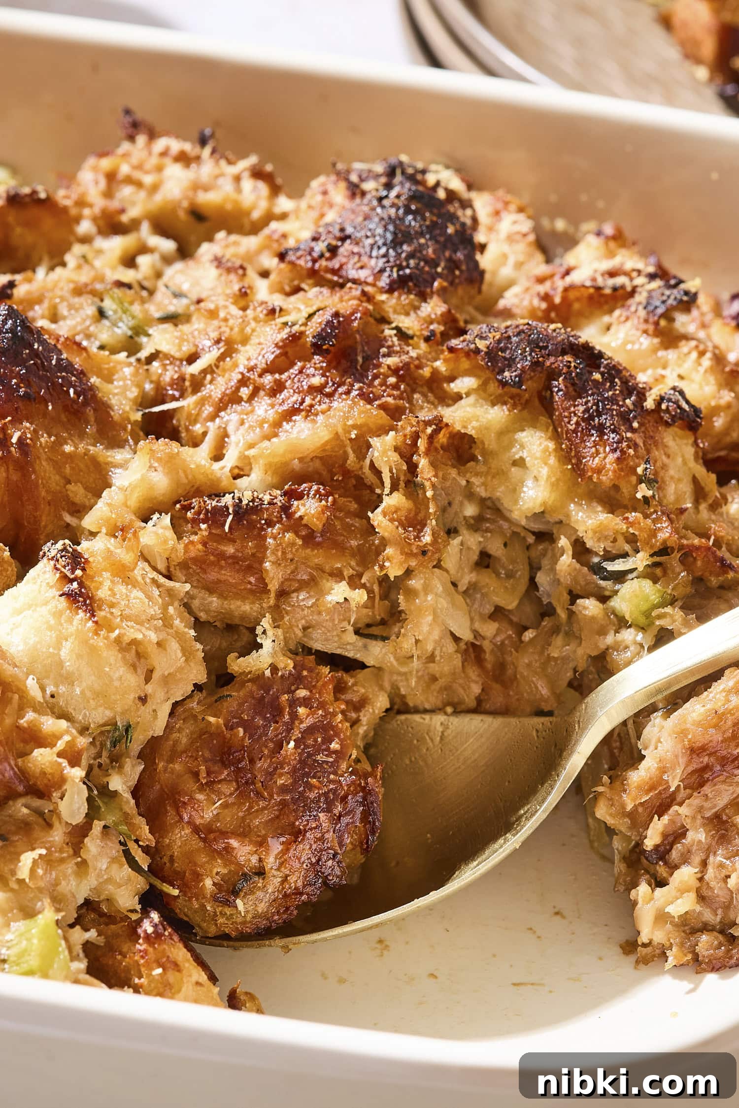 Caramelized Onion and Croissant Stuffing Recipe 14 Spoon scooping up a serving of browned croissant stuffing in a baking dish.