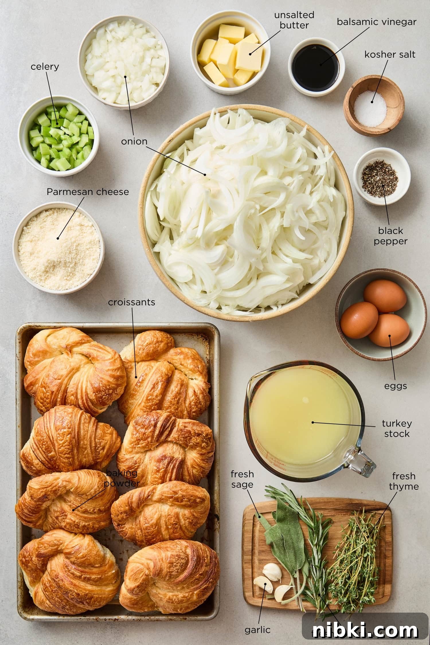 Caramelized Onion and Croissant Stuffing Recipe 5 Concrete surface with ingredients needed for croissant stuffing including croissants, Parmesan cheese, onions, and aromatics.