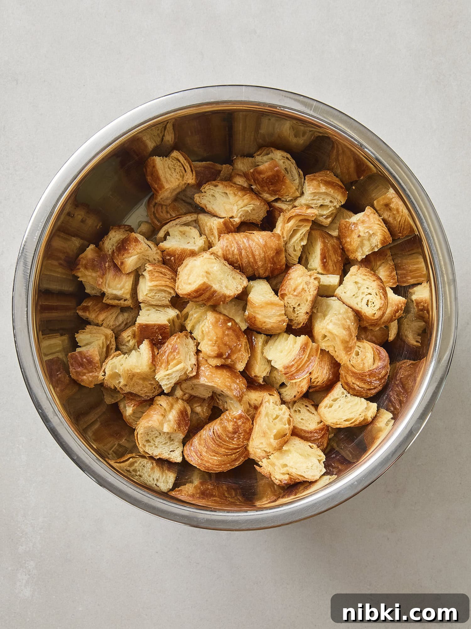 Caramelized Onion and Croissant Stuffing Recipe 10 Metal bowl filled with toasted croissant pieces torn into cubes.