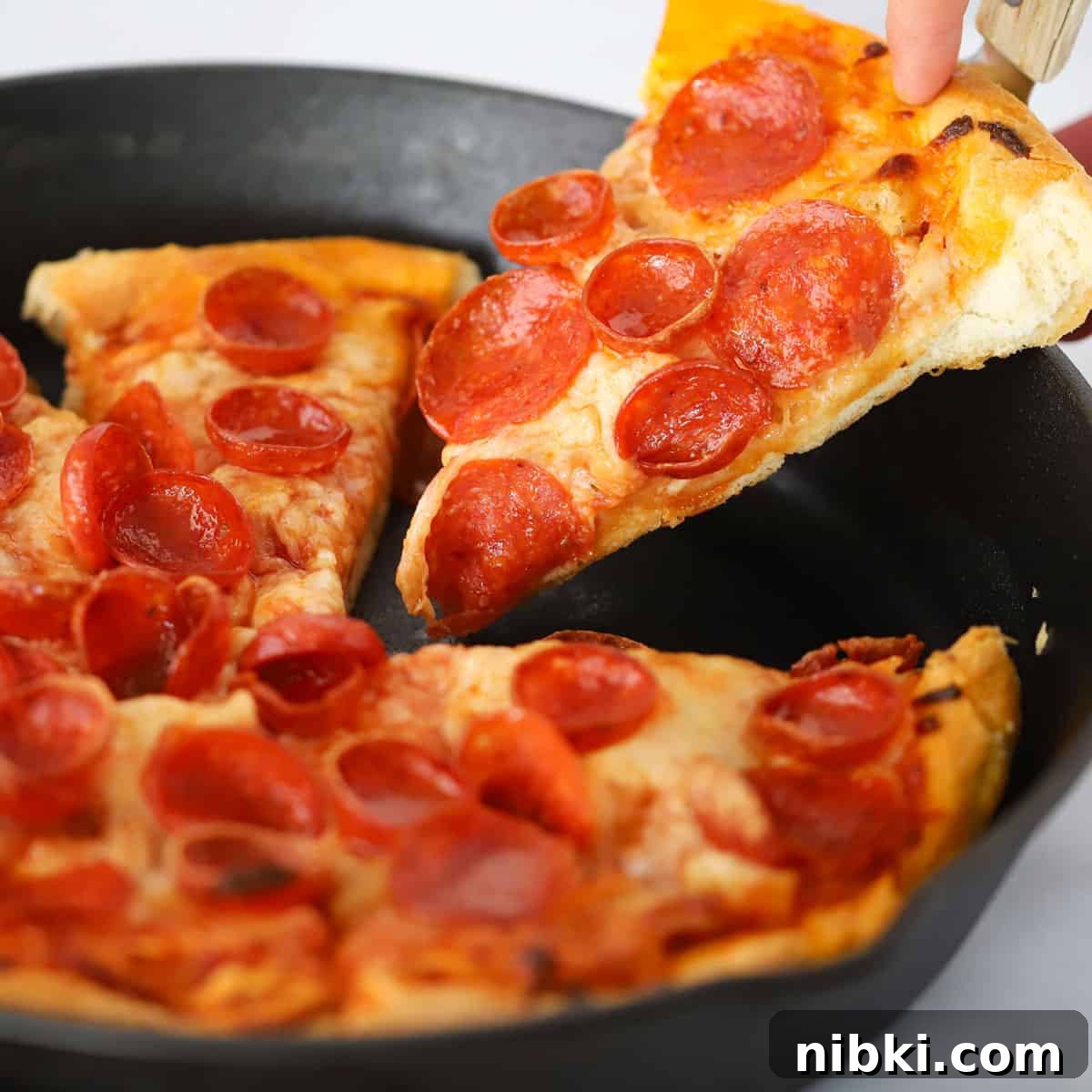 A hand removing a slice of deep dish pizza inside a cast iron skillet.