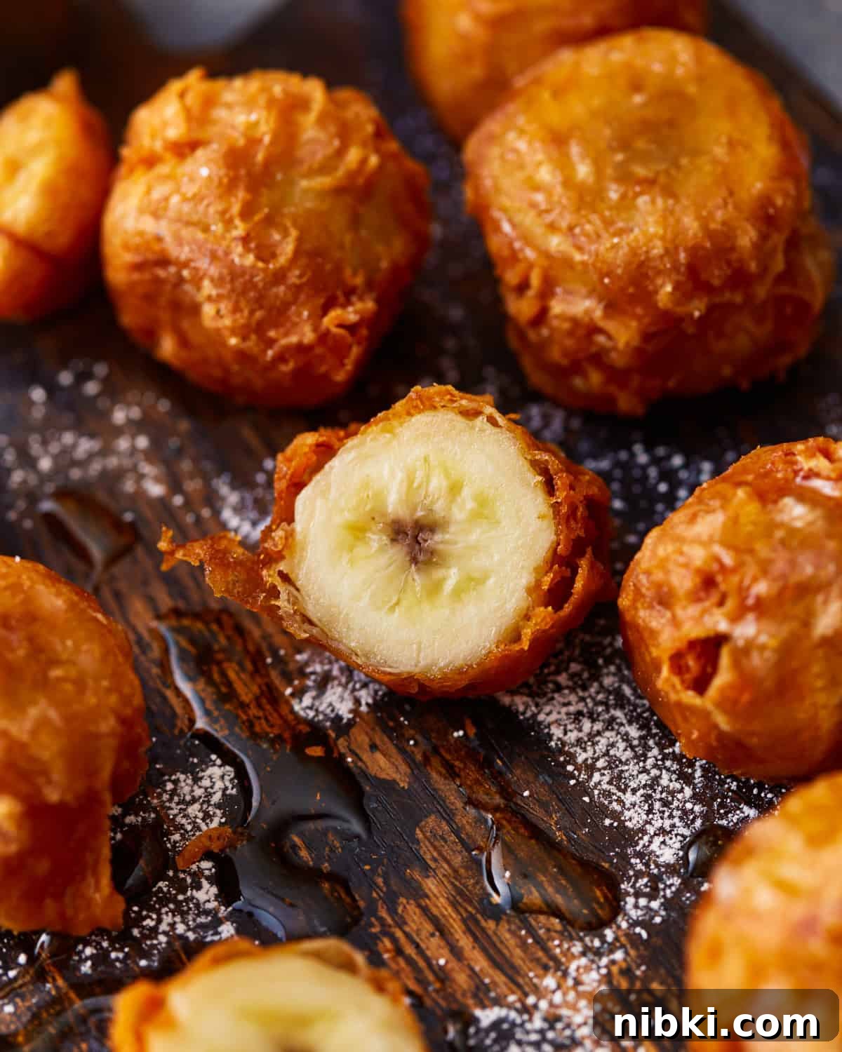 Crispy Fried Banana Fritters Recipe with Cinnamon Sugar 2 Fried bananas dusted with powdered sugar and one cut in half.