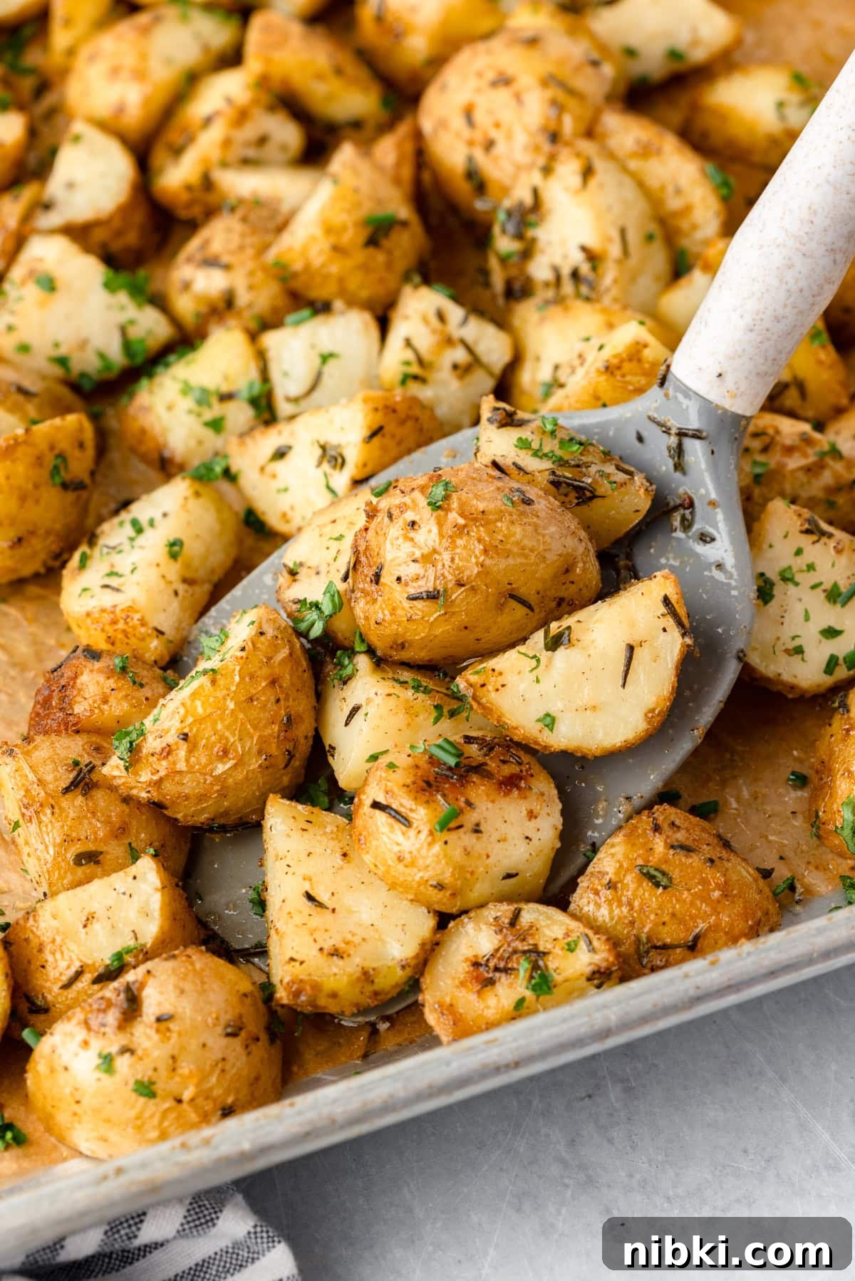 A close-up of roasted potatoes garnished with chopped herbs on a baking sheet.