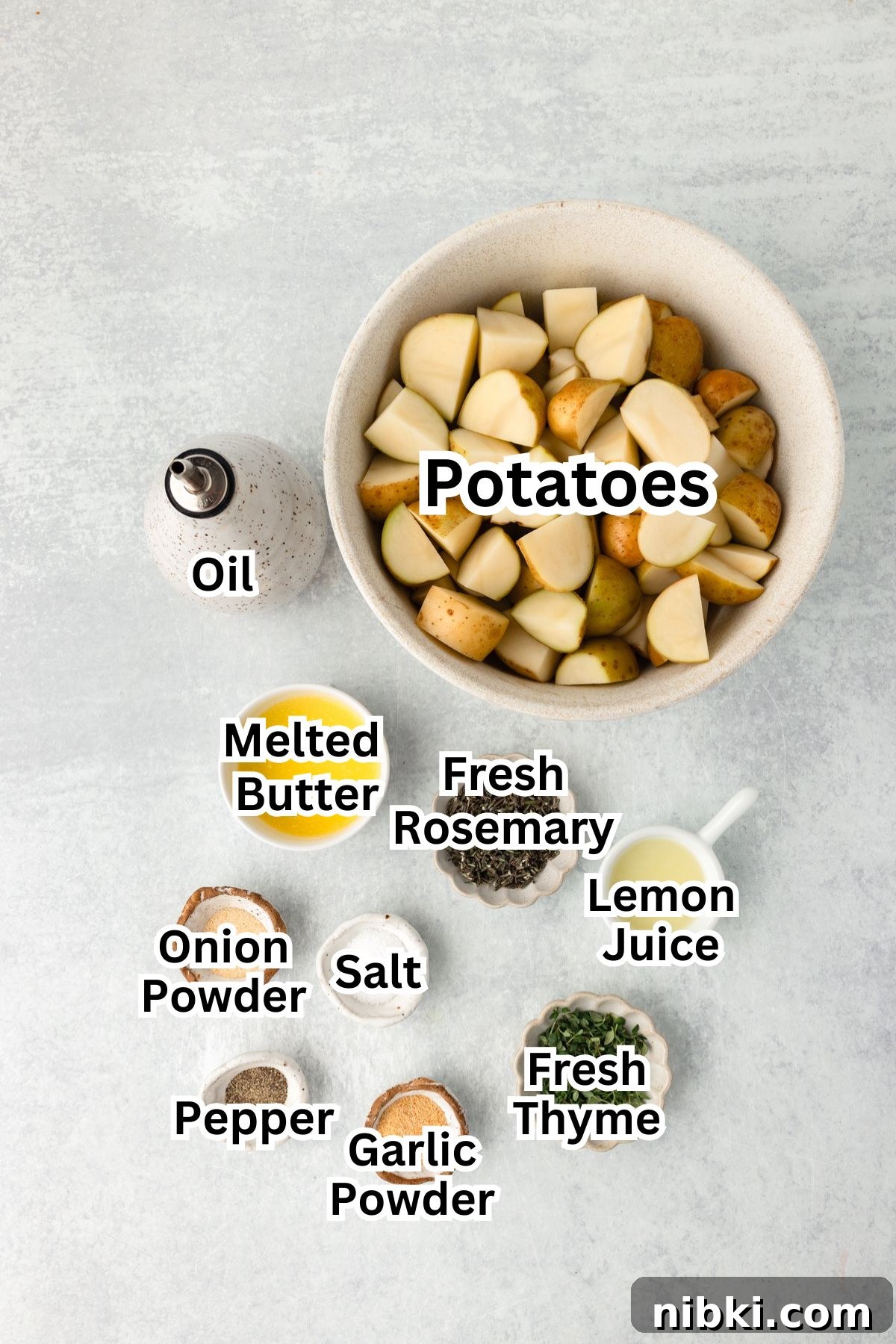 A top-down view of ingredients for roasted potatoes, including a bowl of cut potatoes, oil, melted butter, fresh rosemary, fresh thyme, lemon juice, onion powder, salt, pepper, and garlic powder, all labeled.
