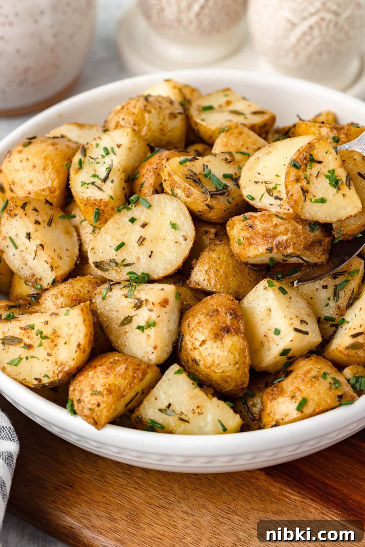A white bowl filled with herb roasted potatoes in a white bowl.