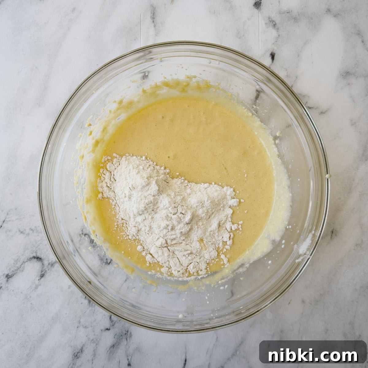 Gluten-Free Strawberry Shortcake Cake Recipe 8 Golden cake batter in a glass bowl with flour being mixed in.