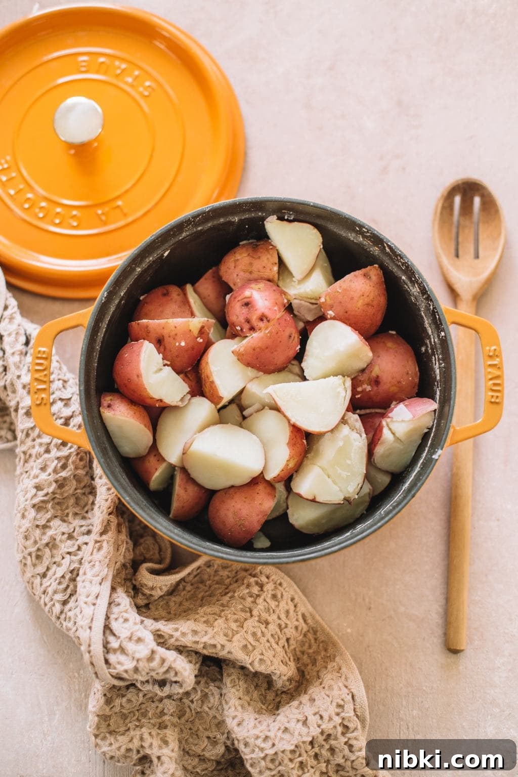 cubed red potatoes in yellow dutch oven with tan kitchen towel and wooden spoon