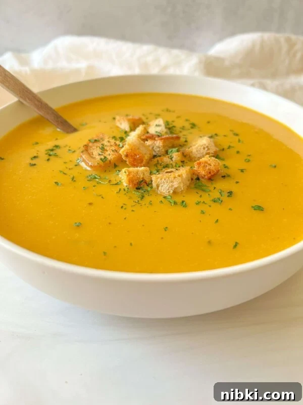 A bowl of creamy orange cream of zucchini soup topped with croutons and herbs.
