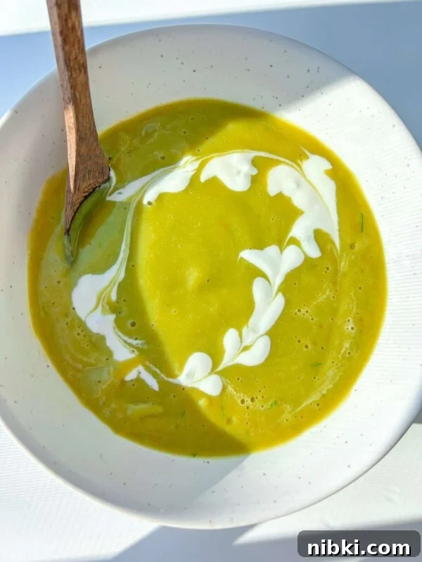 A bowl of healthy cream of broccoli soup with a swirl of cream, served with a wooden spoon.