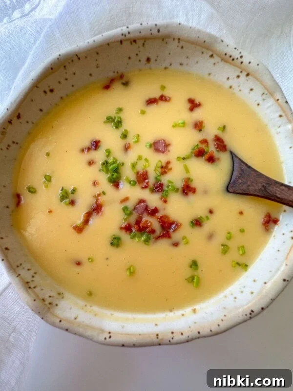 Creamy Garden Vegetable Soup Recipe 2 A bowl of creamy yellow soup garnished with chopped green herbs and crispy bacon bits