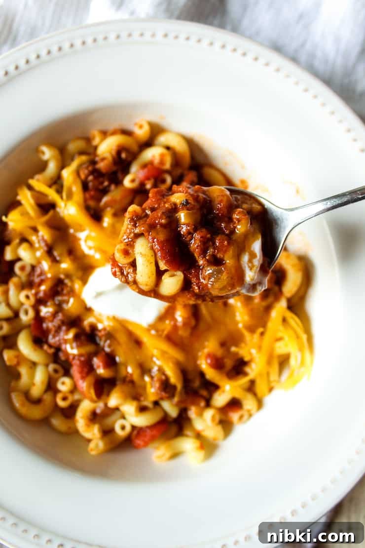 Homestyle Cheesy Chili Mac with Ground Beef and Pasta 2 Chili mac on spoon above bowl.