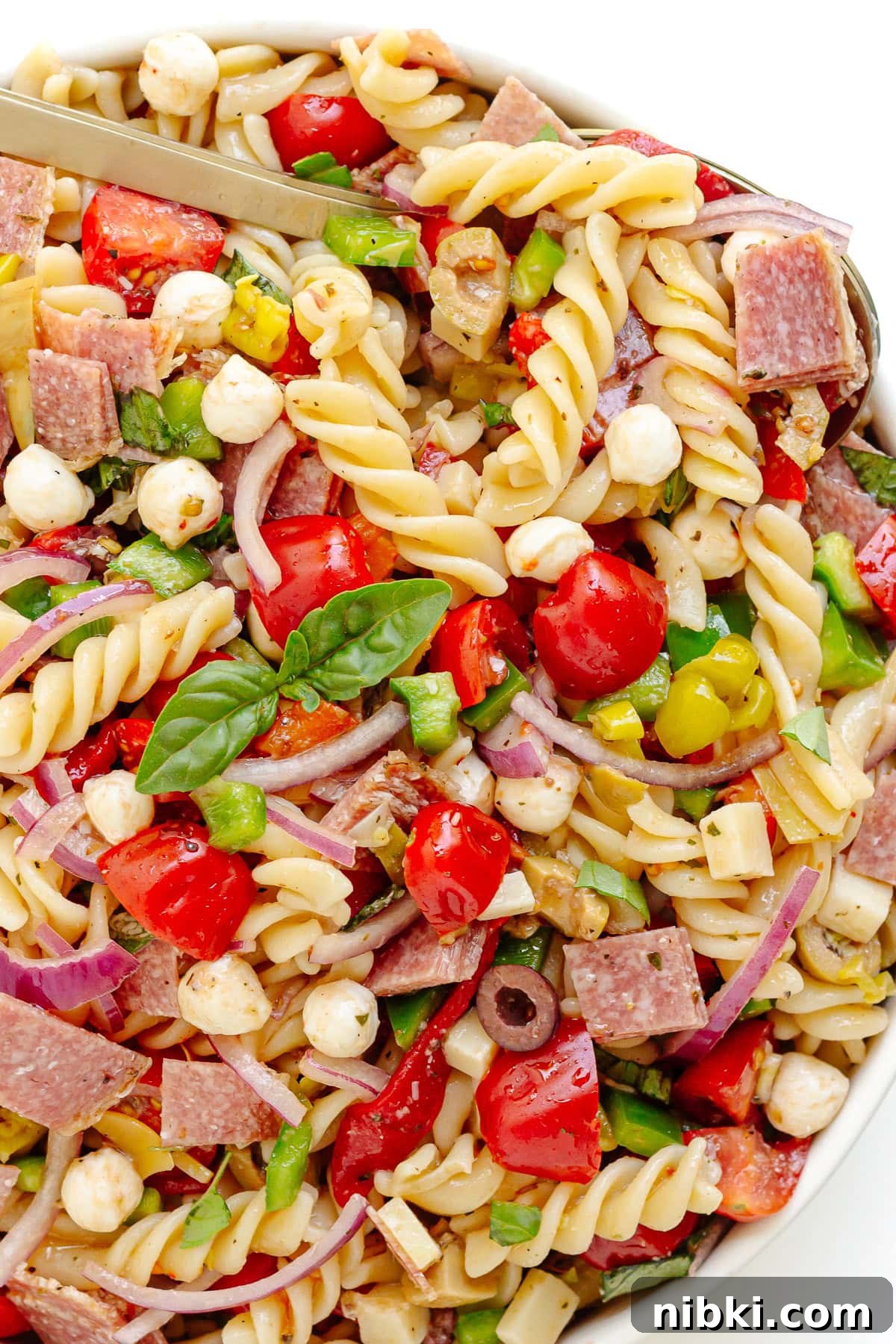 Antipasto Pasta Salad Recipe with Zesty Italian Dressing 3 Italian pasta salad in a white serving bowl with serving spoon scooping some up.