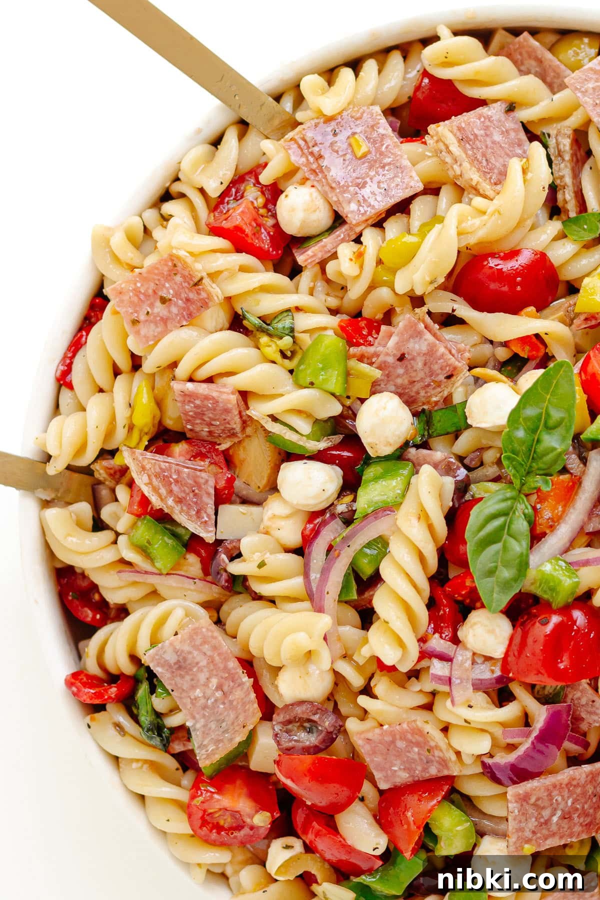 Antipasto Pasta Salad Recipe with Zesty Italian Dressing 7 Salad servers sticking out of a bowl of antipasto pasta salad with zesty Italian dressing.